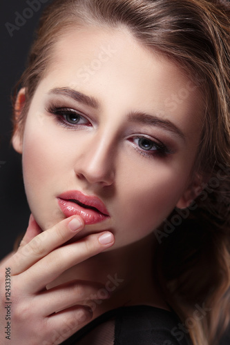 Fashion beauty portrait of a beautiful young girl with a finger at lips on a black background.