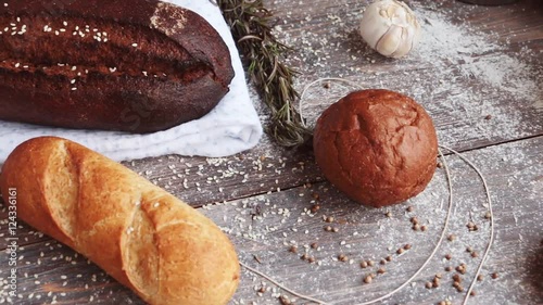 Different types of bread on wooden table dusted with flour. Slow pan. photo