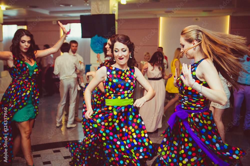 Happy bridesmaids dance on the dancefloor in their light spotted
