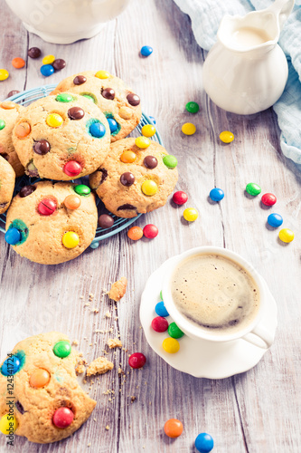 Homemade cookies with colorful chocolate candies with cup coffee on old white wooden table. Retro style toned.