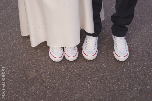bride and groom in white and red gumshoes stand side by side