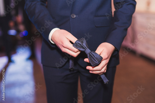 Caucasian guy in suit holding bow tie in his hands