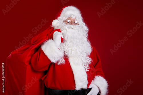 Santa Claus comes with a big bag of gifts. Full length portrait.