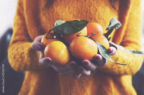 Woman in yellow knitted pullover with ripe clementines in her ha