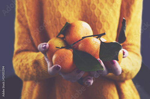 Woman in cozy knitted pullover with fresh clementines in her han