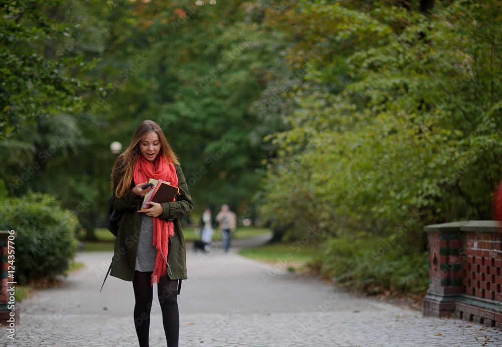 Young student walks in the autumn Park with a mobile phone in hand.