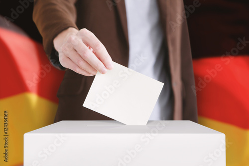 Voting. Man putting a ballot into a voting box with German flag on background.