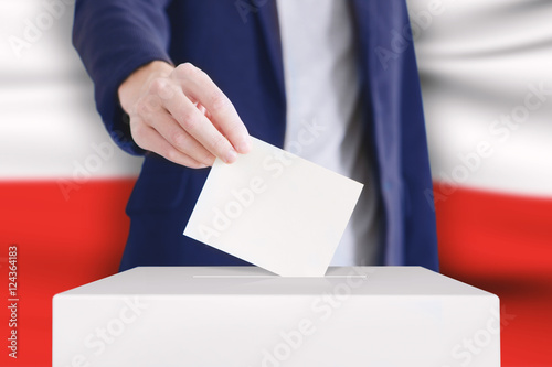 Voting. Man putting a ballot into a voting box with Polish flag on background.