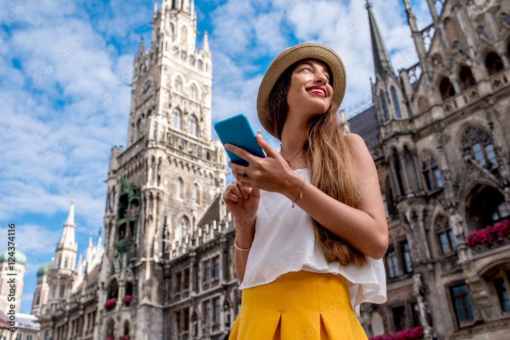 Young female tourist using mobile phone on the central square in front of the famous town hall building in Munich