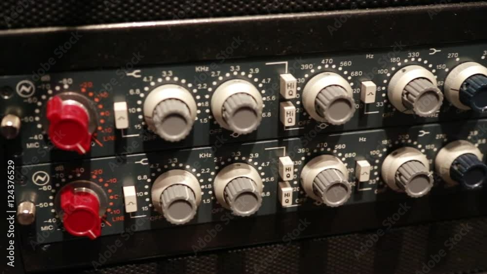Steadicam close up shot of knobs on an audio compressor in a music studio.