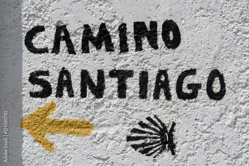 Gelber Pfeil und Aufschrift Camino Santiago auf weisser Mauer in Spanien