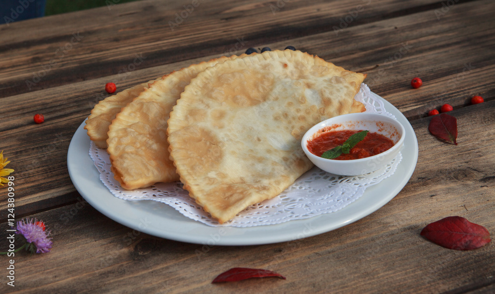Chibureks (meat patties) on wooden table with tomato sauce
Chibureks (meat patties) on wooden table with tomato sauce