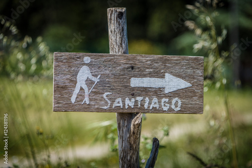 Schild aus Holz mit weisem Pfeil, Symbol eines Pilgers und Aufschrift Santiago am Jakobsweg in Spanien photo