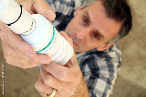 Obraz na plátně Man fitting a low energy CFL light bulb to replace an old-fashio