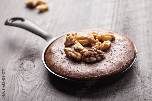 Chocolate brownie topped with walnuts in a cast iron skillet on light brown wooden background