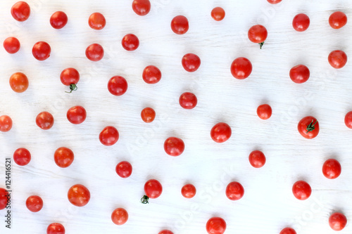 many small red vegetables/ flat lay tomatoes from spilling on light wood surface top view 