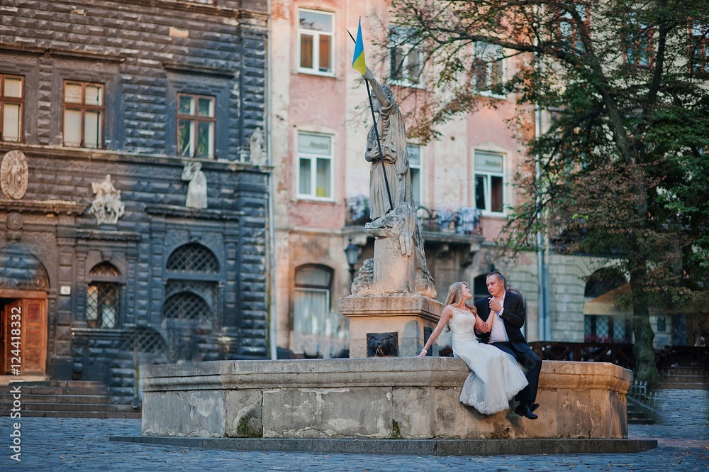 wedding couple siting on oldest monument on city Lviv