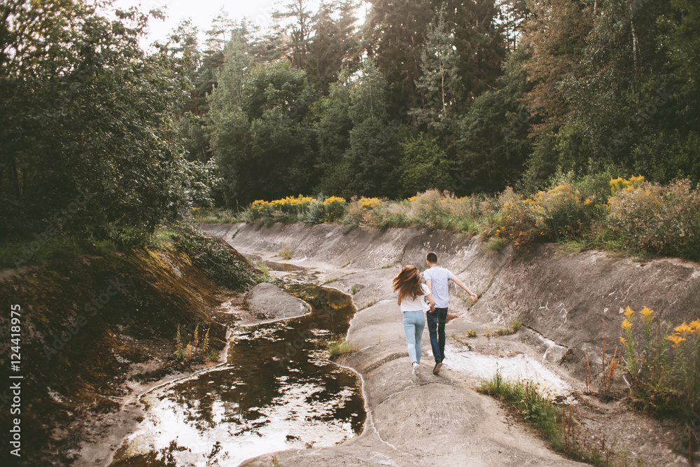 Young couple running near the river and rocky shore