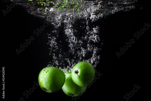 Three green apples splashing into water on black background. Copy space.