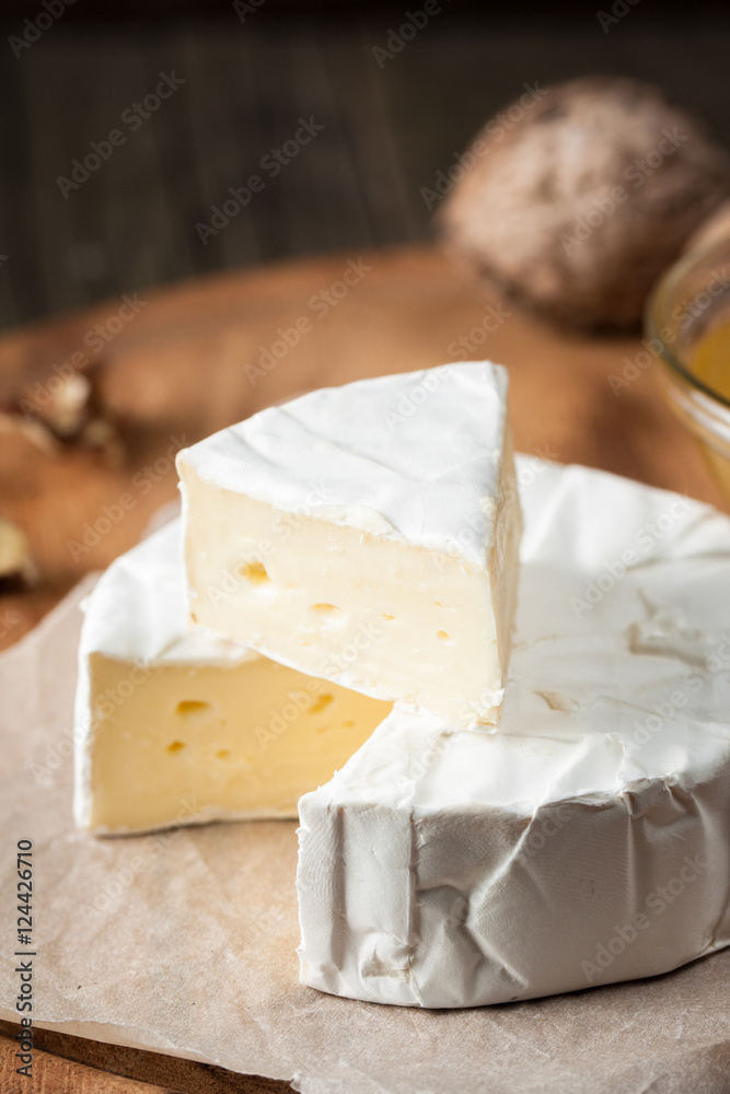 Brie type of cheese. Camembert cheese. Fresh Brie cheese and a slice on a wooden board with nuts, honey and leaves. Italian, French cheese.