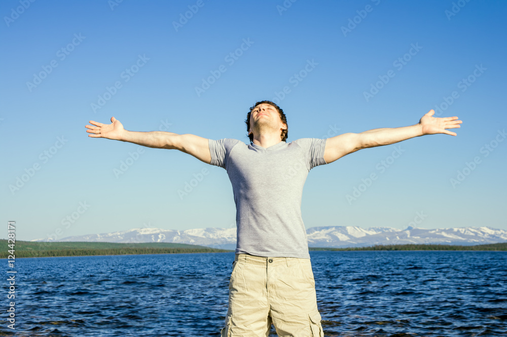 Man traveller standing outdoor with his hands raised to the blue sky northern landscape mountain and sea on background Freedom and Happiness emotional concept Man traveller standing outdoor with his hands raised to the blue sky northern landscape mountain and sea on background Freedom and Happiness emotional concept