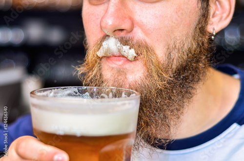 bearded man drinking beer and foam on mustache