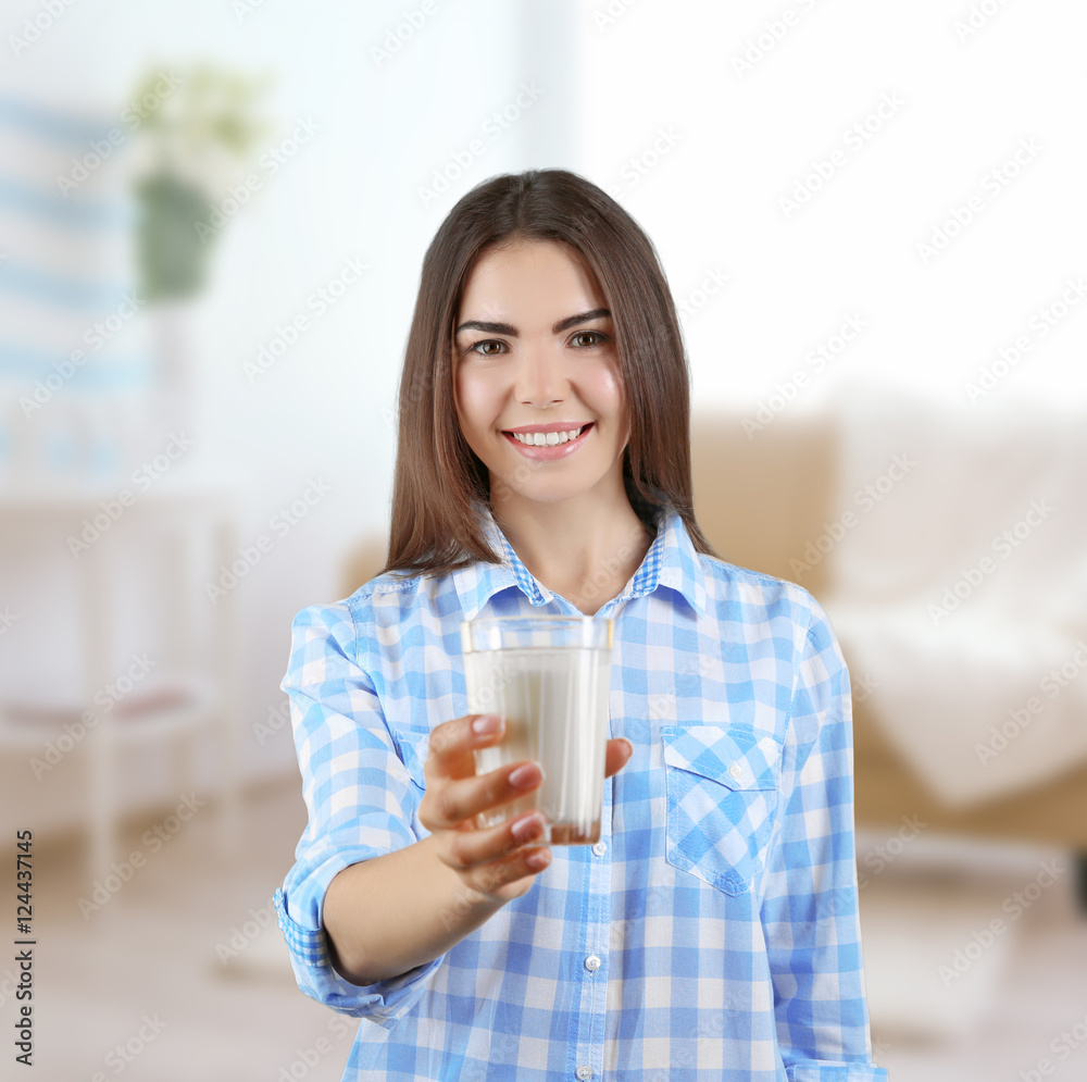 Young woman with glass of milk on blurred interior background.