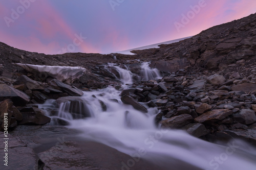 River of melt water from glacier and pink sunset background