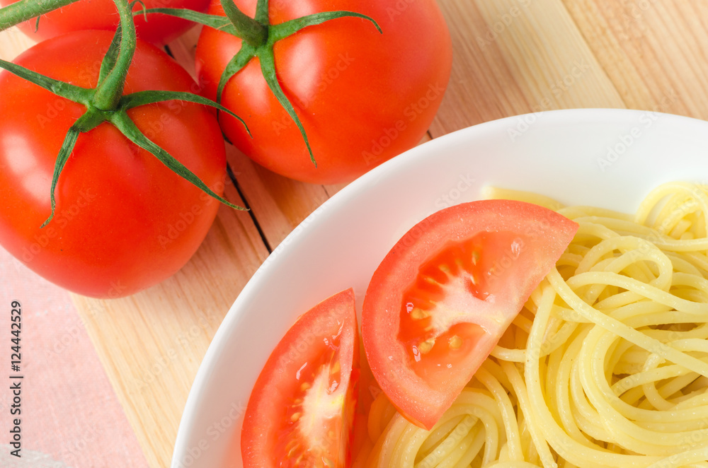plate of tasty pasta with cut tomato and whole tomatoes at background. plate of tasty pasta with cut tomato and whole tomatoes at background.