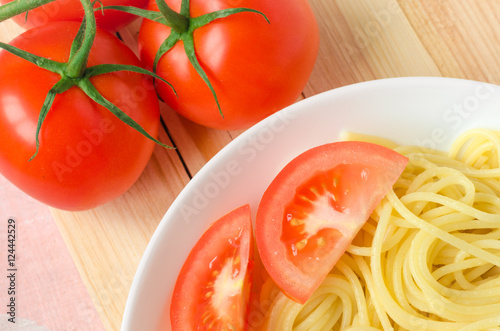 plate of tasty pasta with cut tomato and whole tomatoes at background.