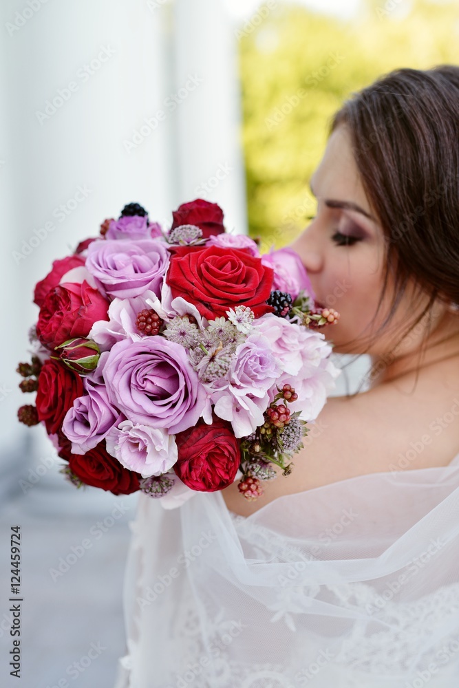 Naklejka premium Beauty bride in bridal gown with bouquet and lace veil in the nature. Beautiful model girl in a white wedding dress. Female portrait in the park. Woman with hairstyle. Cute lady outdoors