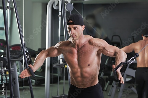 Handsome powerful athletic man doing cable crossover exercise. Strong bodybuilder with perfect abs, chest and arms.