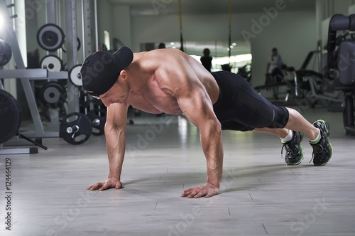 Handsome powerful athletic man performing push ups at the gym. Strong bodybuilder with perfect back  shoulders  biceps  triceps and chest.