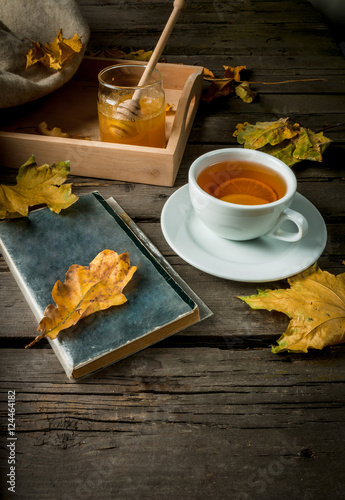 Cozy autumnal mood, warm autumn. A cup of hot tea with lemon and ginger on a rustic table, plaid, yellow leaves, honey and a book to read. Top view © ricka_kinamoto