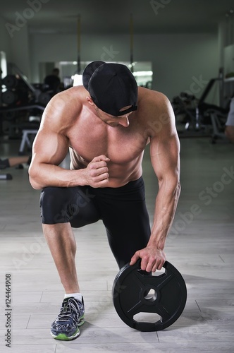 Handsome powerful athletic man preparing for the exercise with weight. Strong bodybuilder with  perfect, shoulders, arms and chest.