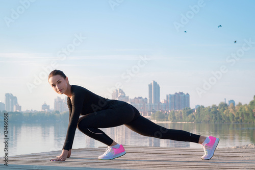 Young pretty woman exercises on pier during morning sport workou photo