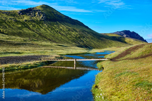 Travel to Iceland. Beautiful Icelandic landscape with bridge over creek, mountains, sky and clouds. Trekking in national park Landmannalaugar