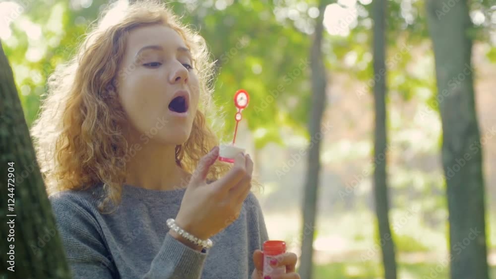 young attractive female blowing soap bubbles in park, portrait, slow motion young attractive female blowing soap bubbles in park, portrait, slow motion