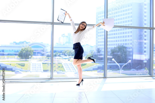 Happy modern business woman with financial report is running in office hall © volha_r