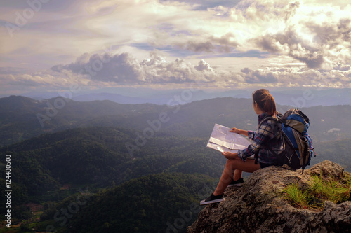 Young woman sitting on hill, looking at map, Hiking and Adventure Concept.
