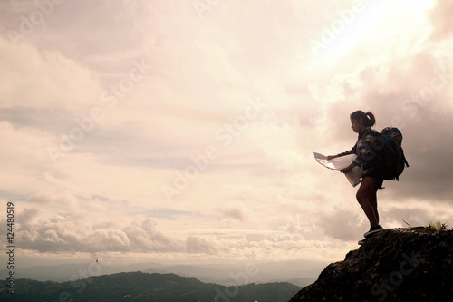 Young woman standing on hill, looking at map, Hiking and Adventure Concept.