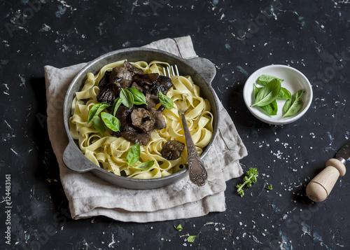 Italian pasta tagliatelle with wild mushrooms in a frying pan on a dark background. Delicious vegetarian food