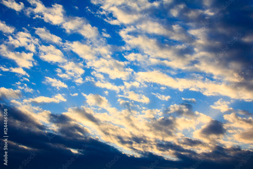 White fluffy clouds in blue sky at sunset, sky background.