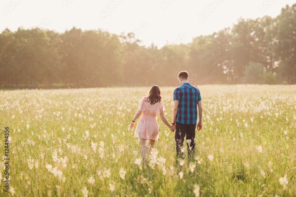 young couple walking in the blooming field with flowers in sunlight