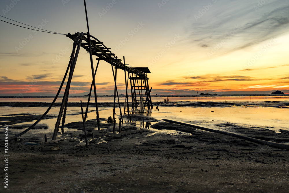 Golden Hour moment,beautiful tropical sunset background, wooden water pump tower on the muddy beach. cloudy and yellow sky.surface level shot.low tide sea view Golden Hour moment,beautiful tropical sunset background, wooden water pump tower on the muddy beach. cloudy and yellow sky.surface level shot.low tide sea view