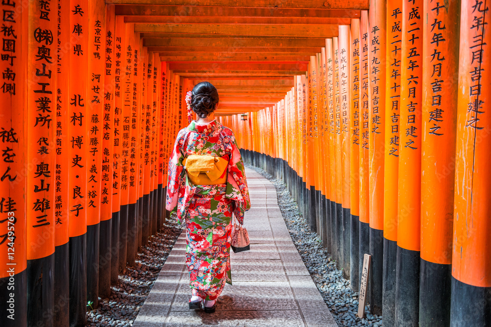 Fototapeta premium Women in kimono stand at Red Torii gates in Fushimi Inari shrine, one of famous landmarks in Kyoto, Japan