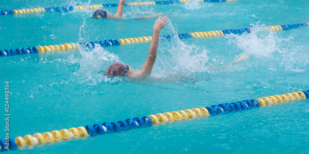 Competitive swimming with events in backstroke. Boys are swimming in a race. Focus on water splash, some motion blur.