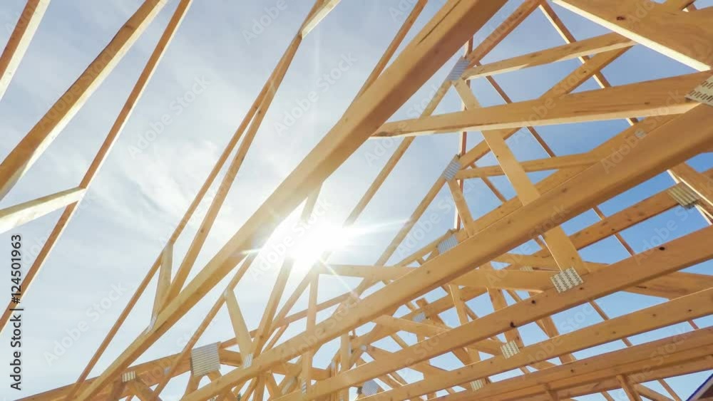 Roof beams of a modern American home in mid construction phase, looking up toward blue sky with sunlight