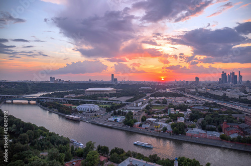 Panoramic view of sunset above Moscow city and cloud reflections in river with traveling boats and bridge