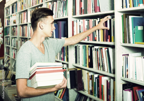 portrait of boy standing among bookshelves and searching for bo